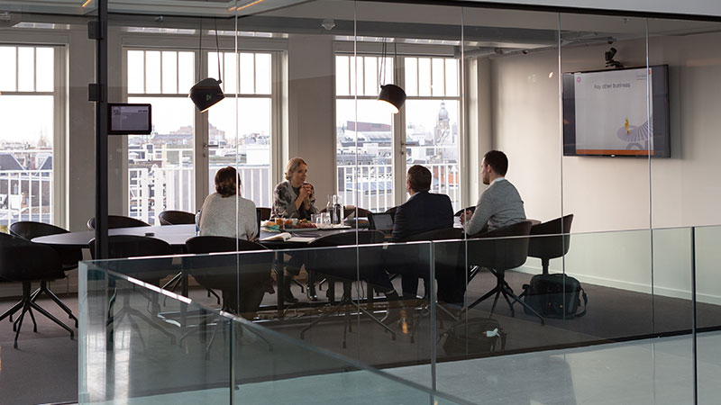 Four coworkers in a conference room happily working at their laptops and talking to one another.